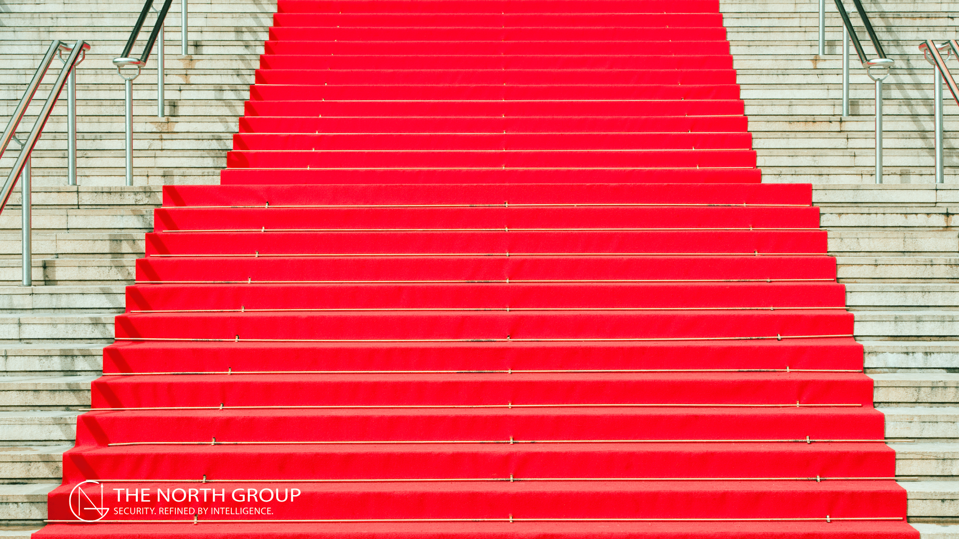 Wide staircase covered with a bright red carpet, flanked by metal railings, with "The North Group" logo at the bottom left corner.