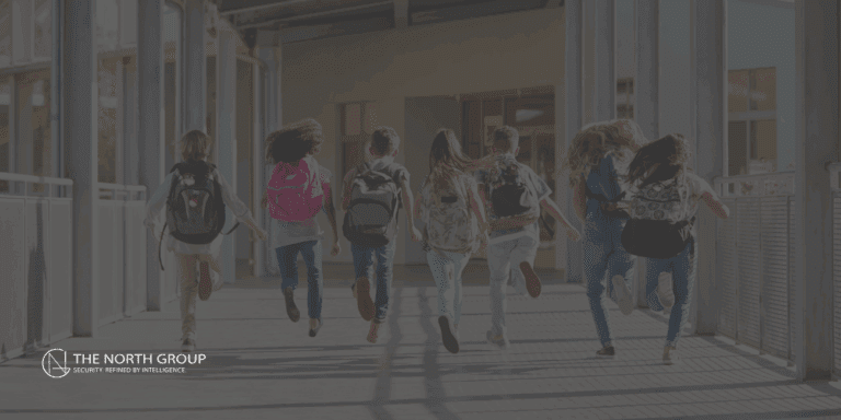 A group of school children with backpacks run across a pedestrian bridge toward a Safe School building on a sunny day. The North Group logo appears in the bottom left corner.